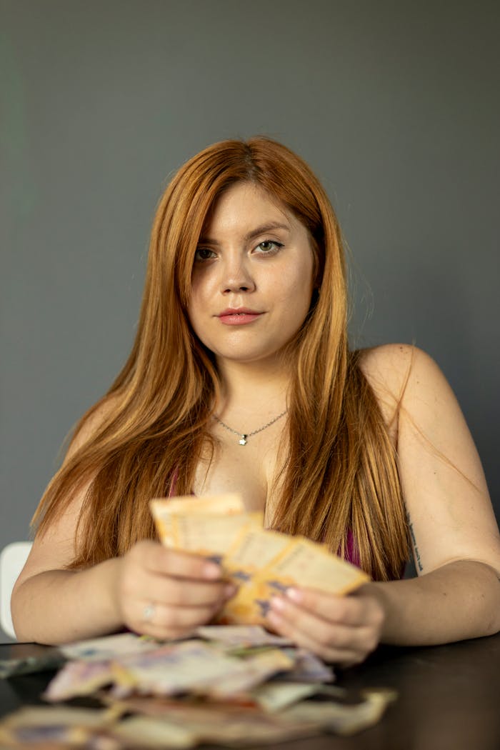 Portrait of a young woman with long hair counting Argentine pesos indoors, Buenos Aires.