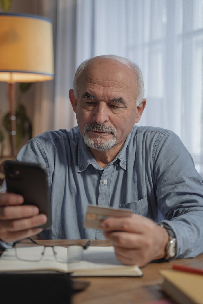Elderly man using mobile phone and credit card at home office for online shopping.