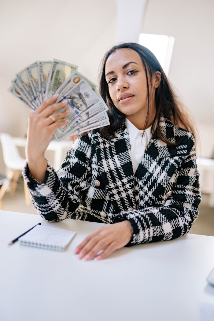 Woman holding American dollars confidently, depicting wealth and success in a bright indoor setting.