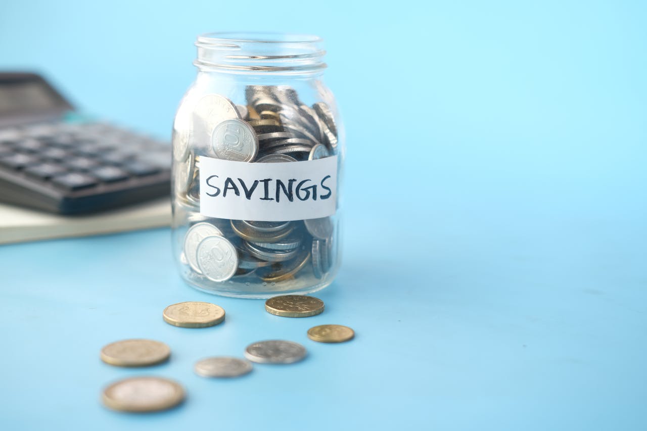 Glass jar labeled 'Savings' filled with coins, beside a calculator on a blue background.